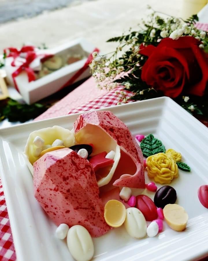 Hollow chocolate heart, broken open to reveal more chocolates inside, next to a rose flower arrangement